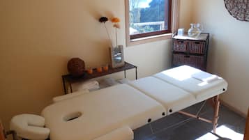 Relax in a serene spa room with a massage table, wicker chair, and tranquil views.