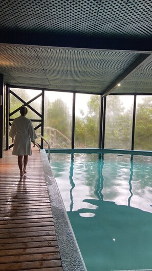A person walking towards a pool with a view of trees through large windows.