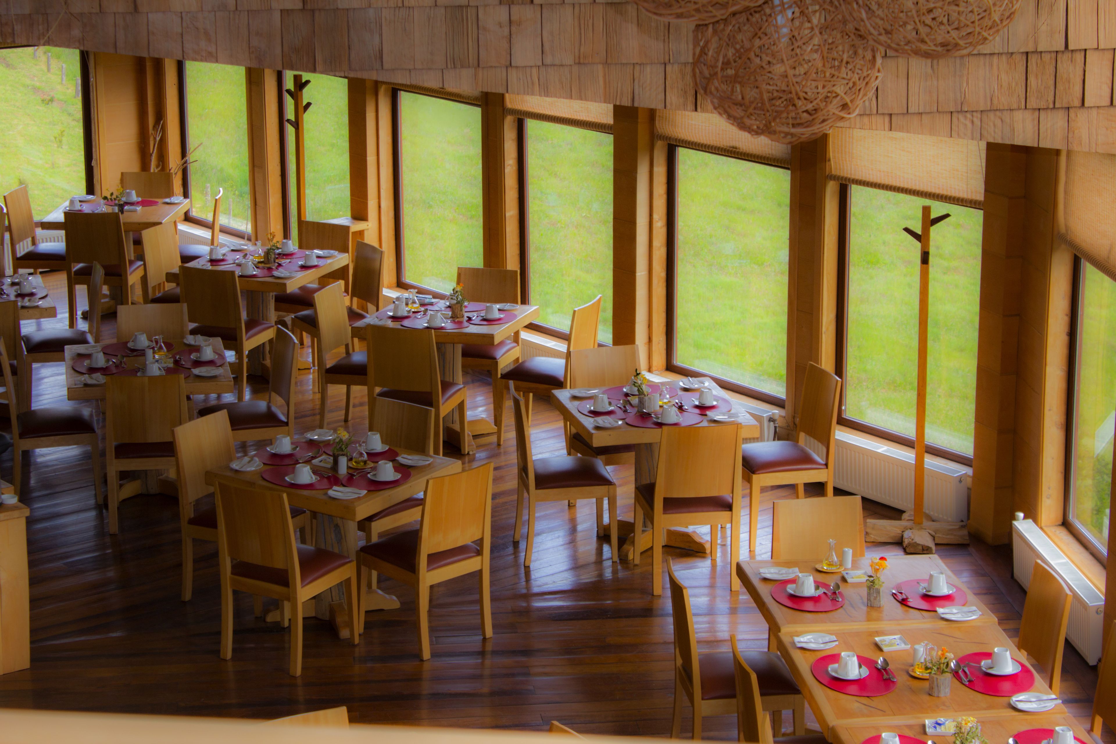 A dining area with multiple tables and chairs, large windows, and a wooden interior.