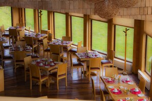 A dining area with multiple tables and chairs, large windows, and a wooden interior.