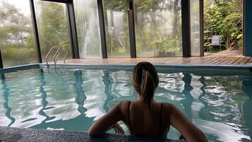 Una persona en una piscina con vistas a árboles a través de amplios ventanales.
