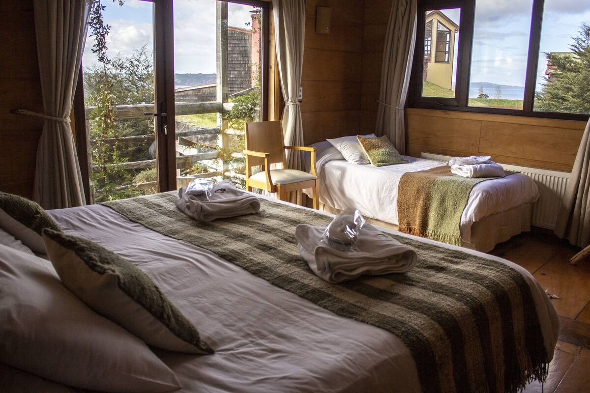 A room with two beds, a chair, and a view of the outdoors.