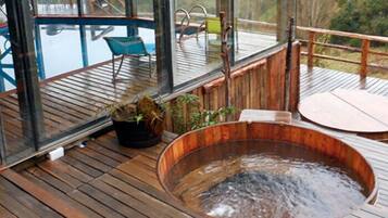 Una terraza de madera con jacuzzi, plantas en macetas y mobiliario exterior.