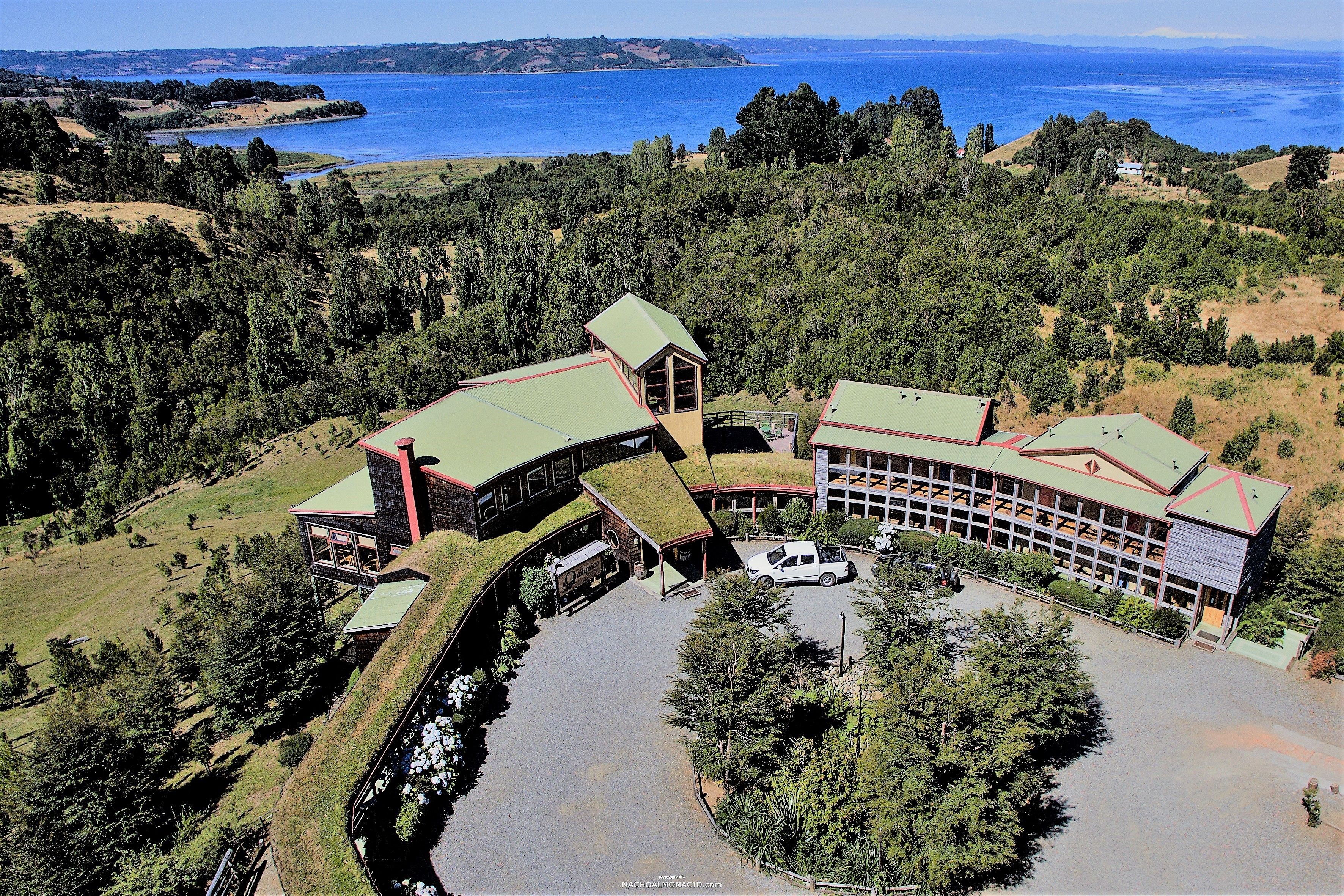 Un edificio grande con techo verde, rodeado de árboles y un lago.