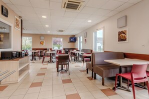 Un restaurante amplio con numerosas mesas y cabinas, una zona de cocina y grandes ventanales que aportan luz natural.