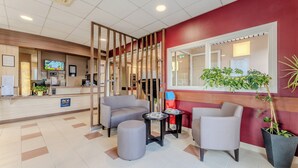 Zona de recepción de hotel con diseño moderno, que incluye un mostrador de recepción, un área de estar con sillas y una mesa redonda, y un ventanal con vistas.