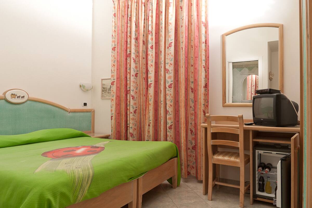A bedroom with a bed, a wooden chair, a television, and a small refrigerator.