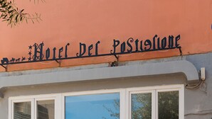 A two-story building with a sign reading "Hotel Del Postiglione." The ground floor has large arched windows with colorful artwork. - Hotel Del Postiglione (Ischia)