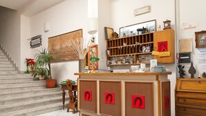 A room with a staircase, a wooden cabinet with red handles, a bookshelf, and a potted plant. - Hotel Del Postiglione (Ischia)