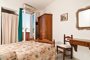A bedroom with a bed, a wooden wardrobe, a desk with a chair, and a mirror on the wall. - Hotel Del Postiglione (Ischia)