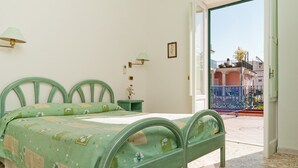 A bedroom with a bed, a nightstand, a lamp, and a view of a blue railing outside. - Hotel Del Postiglione (Ischia)