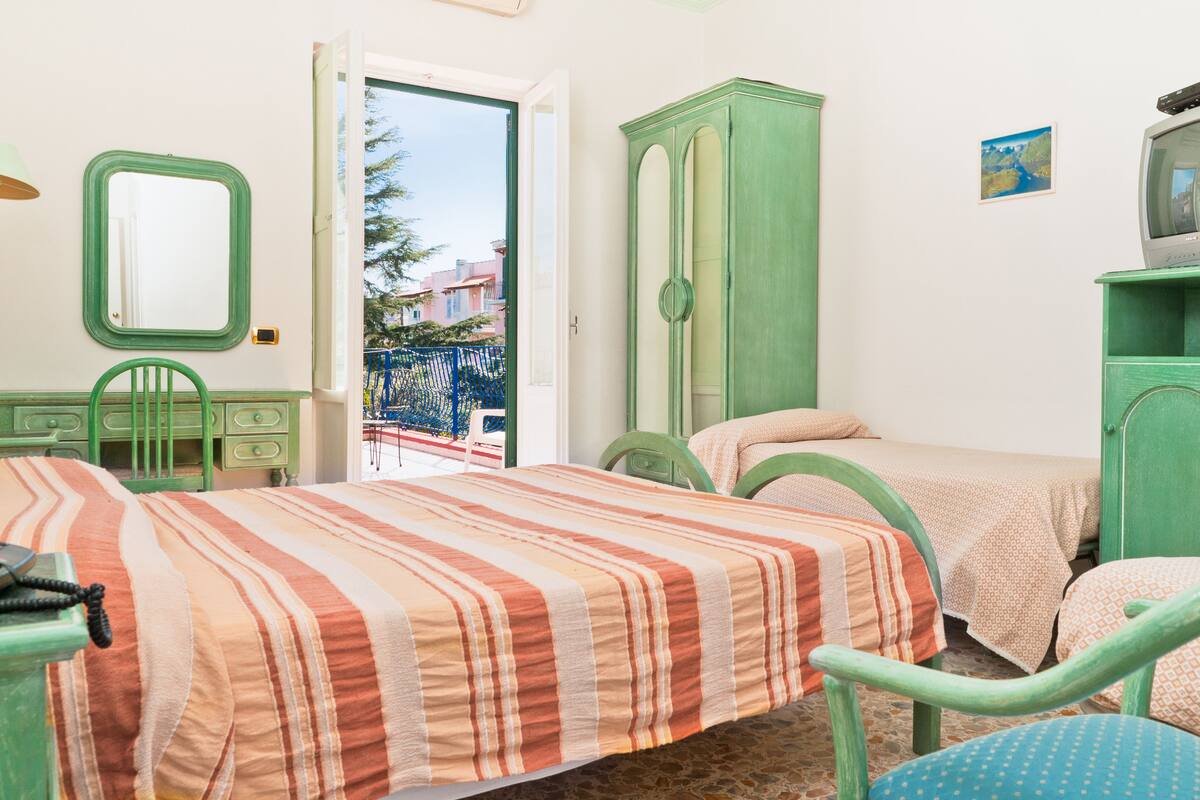 A room with two beds, a green wardrobe, a television, and a small table.