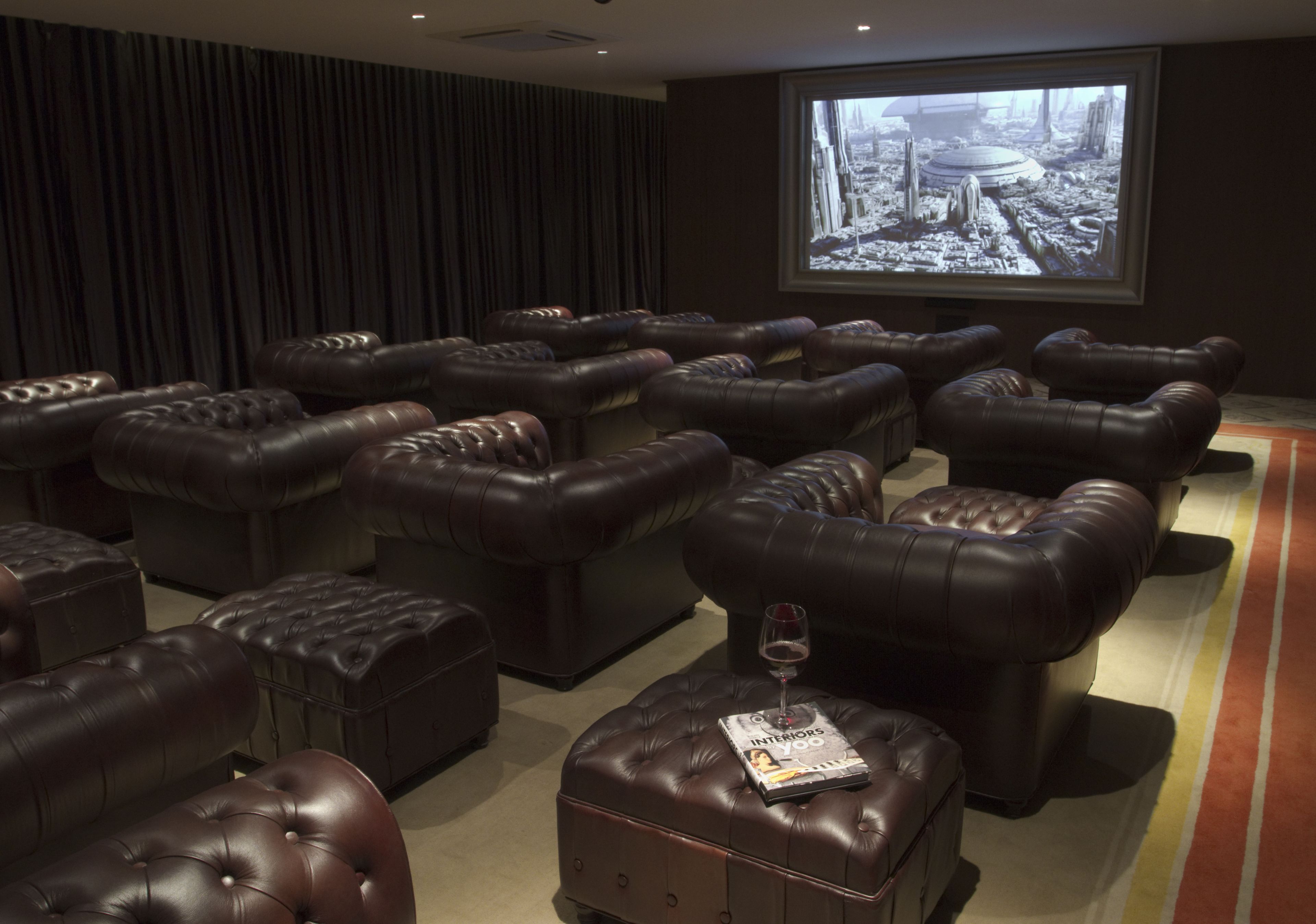 Una sala de cine con varios sillones reclinables de cuero y una pantalla grande mostrando una película.
