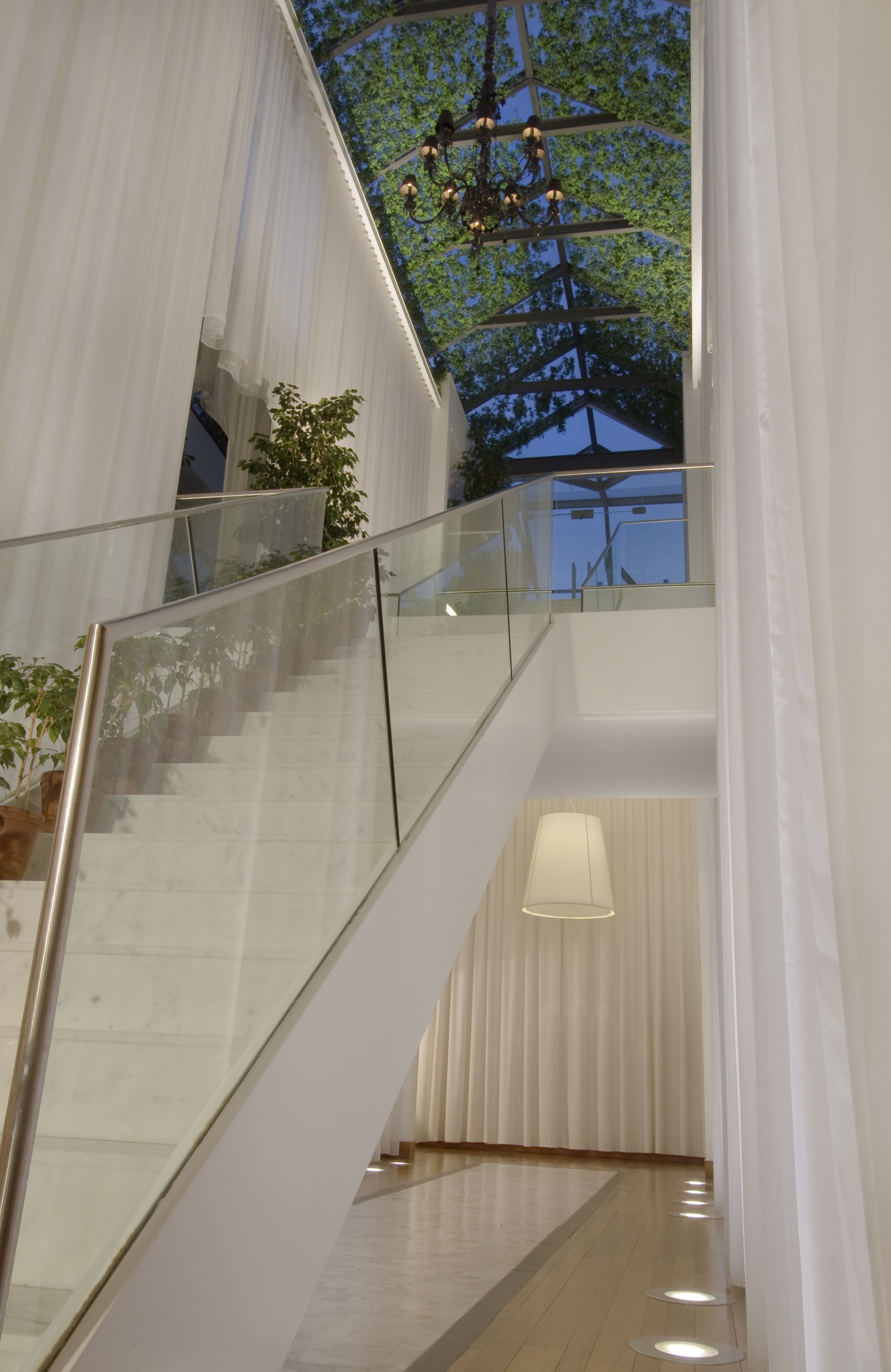 A modern interior with a glass railing staircase, a hanging light fixture, and a view of trees through the ceiling.