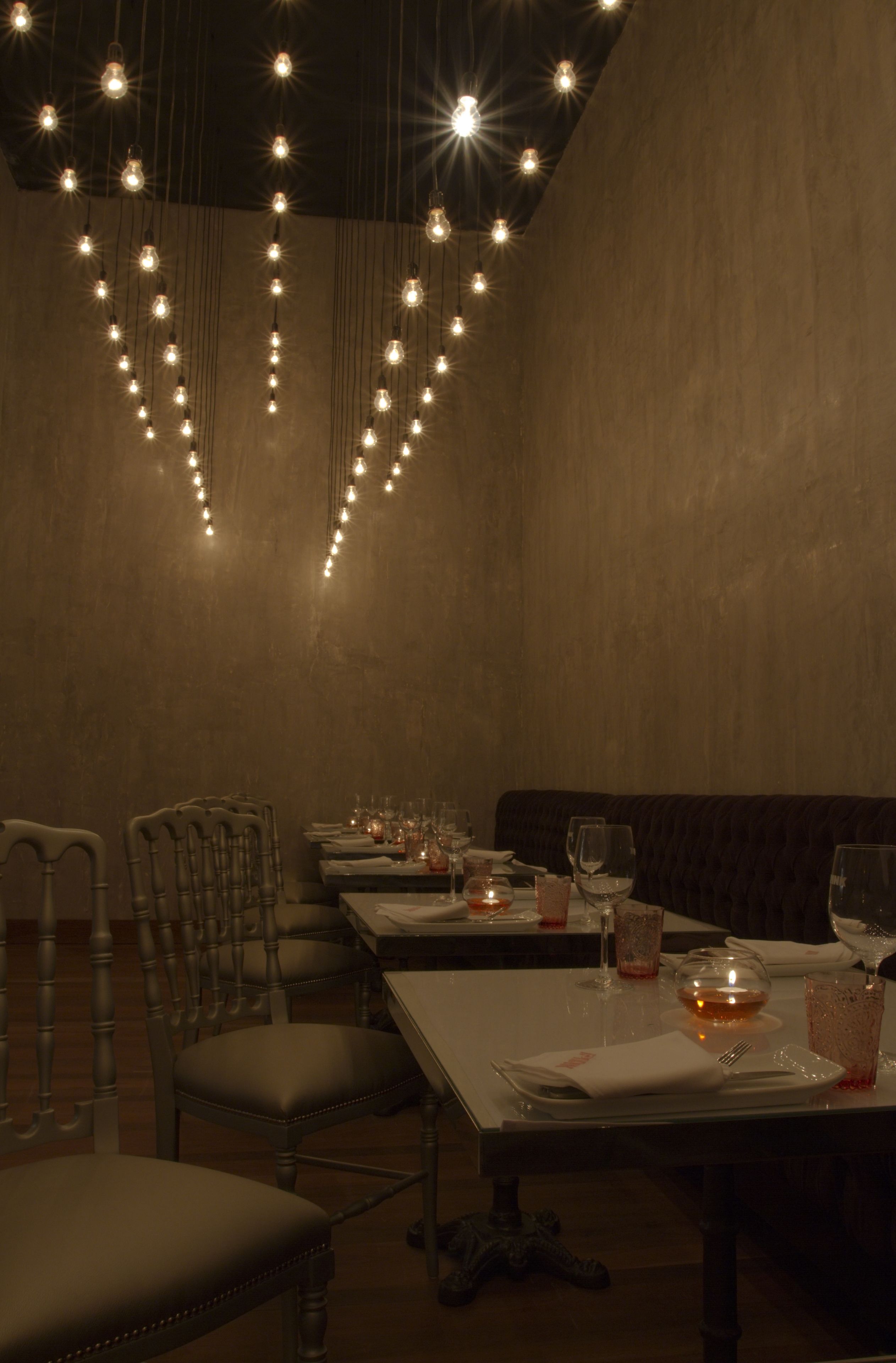 Un restaurante tenuemente iluminado con una larga mesa dispuesta para comer, sillas y un accesorio de iluminación decorativo en el techo.