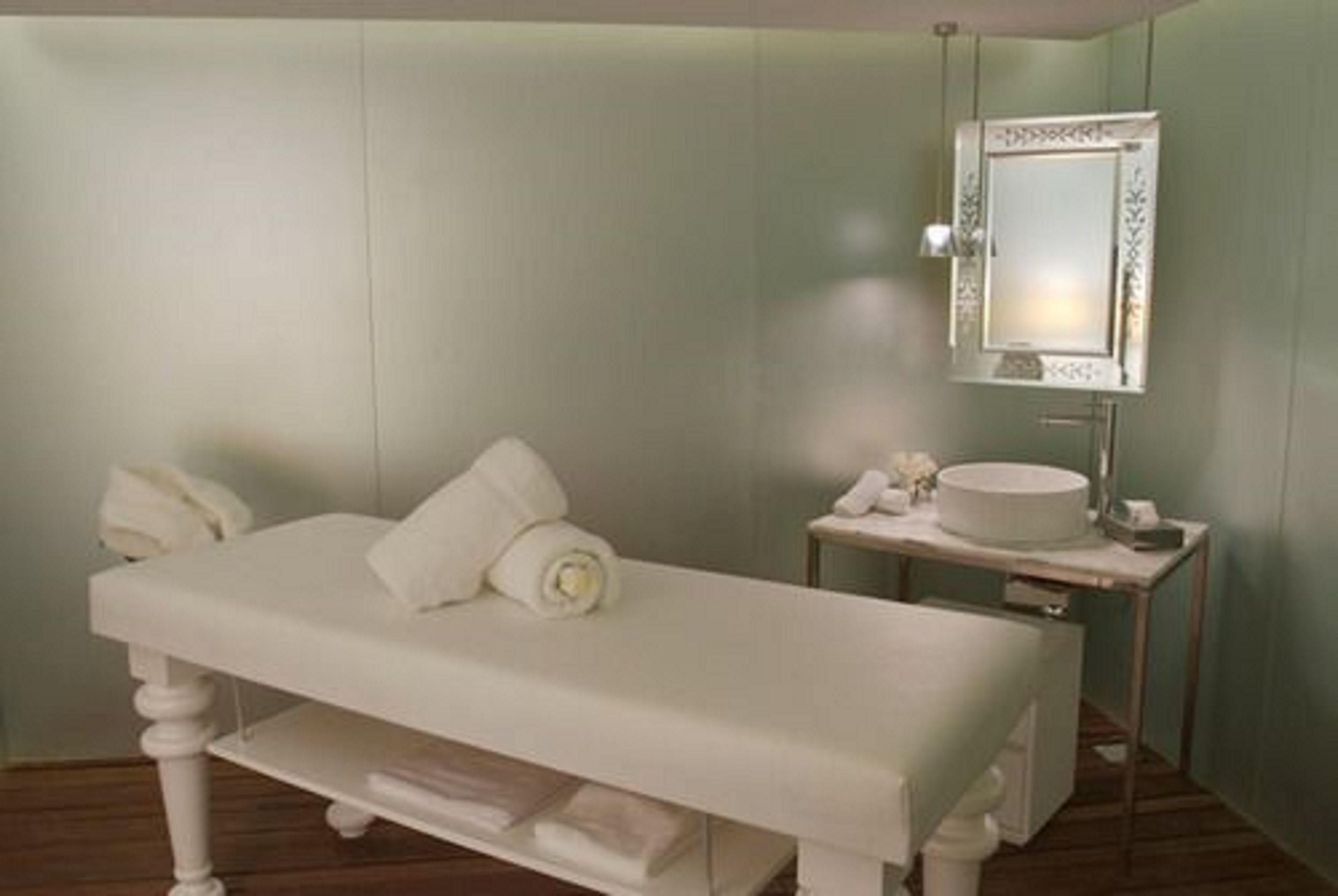 Casa de banho com toucador branco, espelho redondo com moldura decorativa e uma pequena pia.