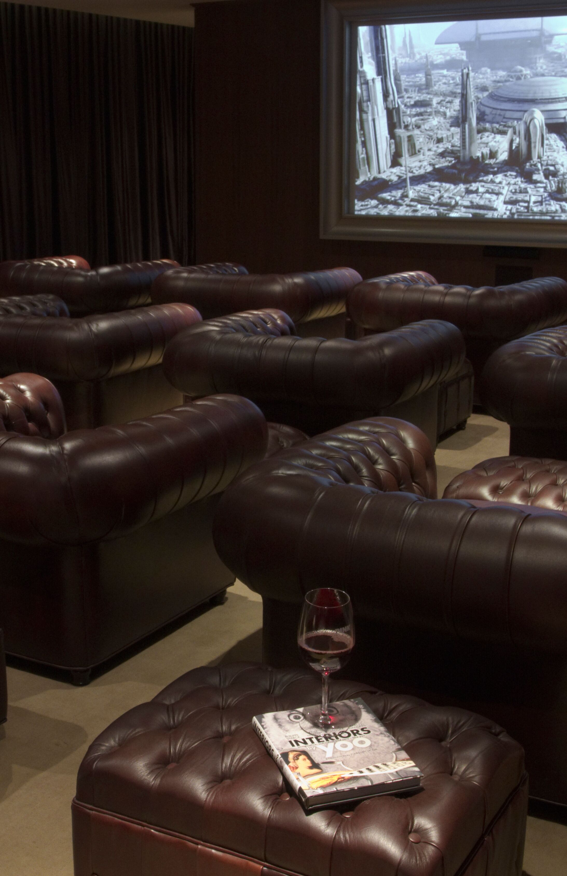 Un cine en casa con sillones reclinables de cuero, una copa de vino y un televisor mostrando un paisaje urbano.