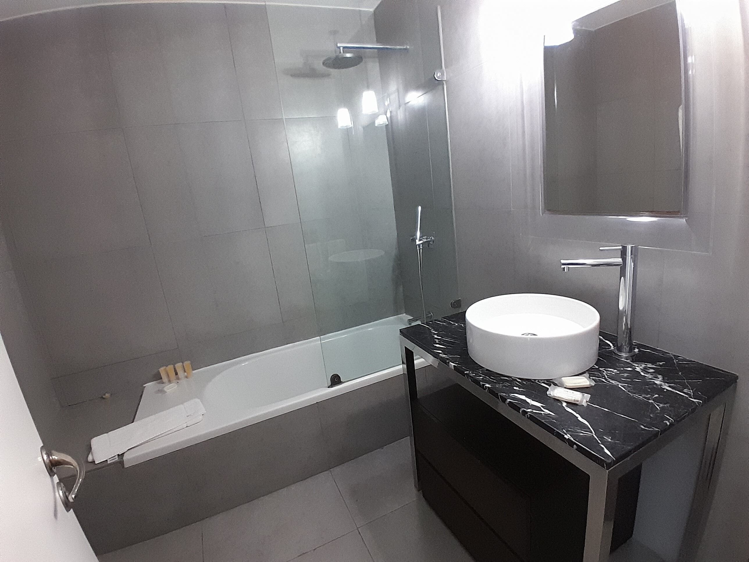 A modern bathroom with a bathtub, a glass-enclosed shower, and a vanity with a white sink and black marble countertop.
