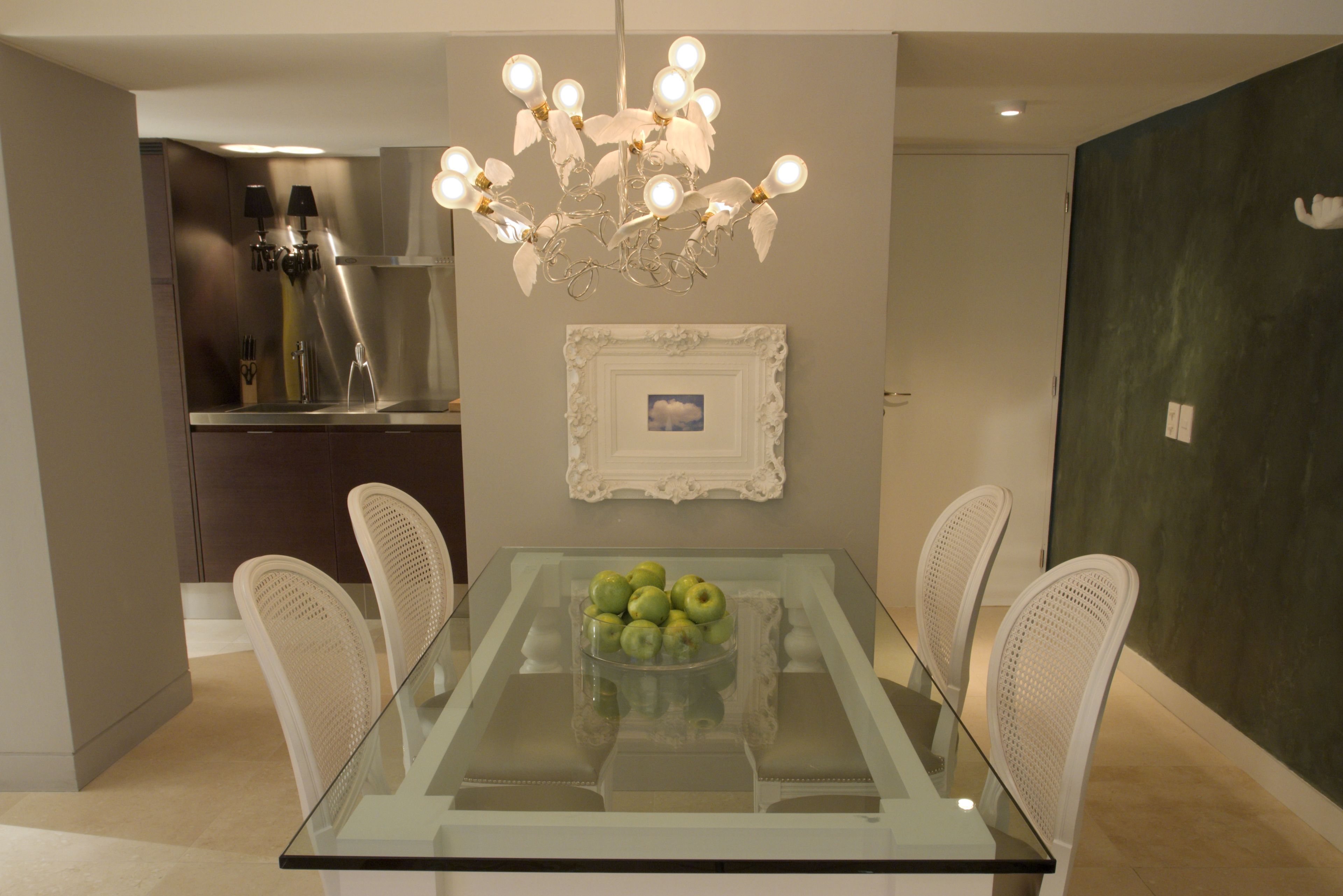 A dining area with a glass table, white chairs, a chandelier, and a framed picture on the wall.