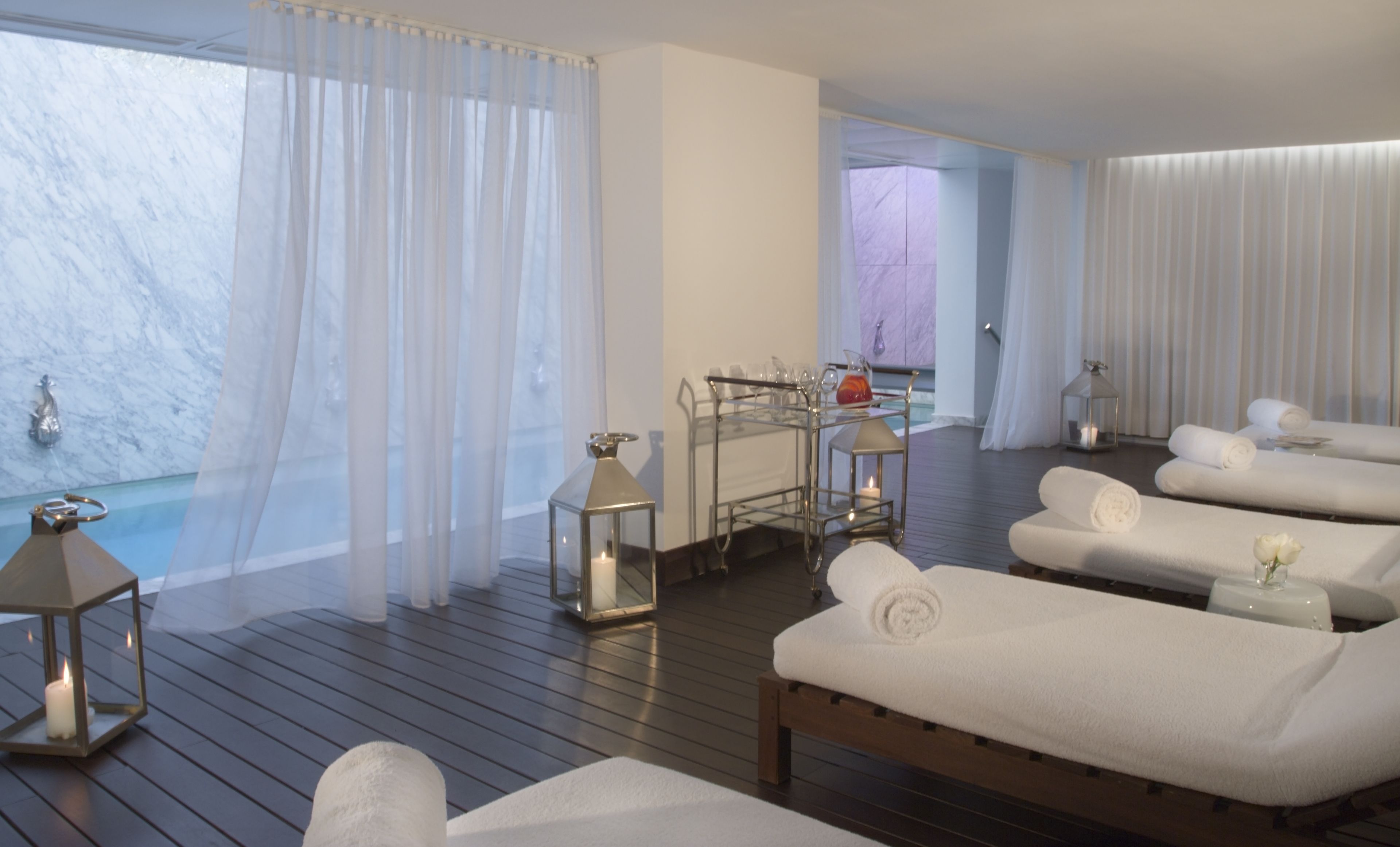 A spa area with wooden loungers, a glass cart with amenities, and a marble wall.