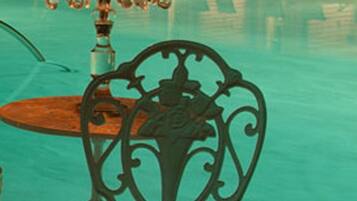 Un área junto a la piscina con una silla y una mesa de hierro forjado, rodeada de sillones de descanso y una fuente iluminada con velas.