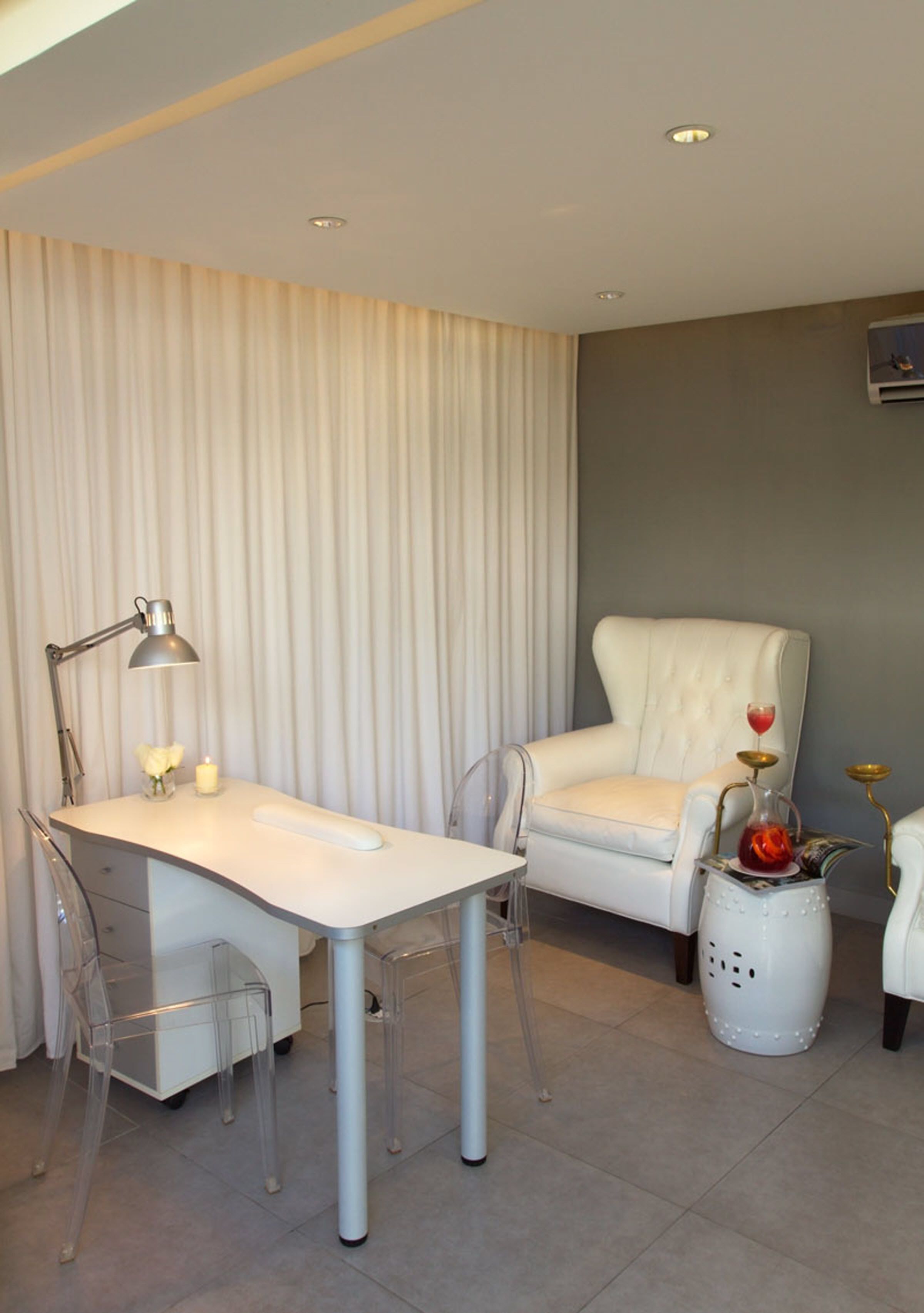 A modern room with a white desk, clear chairs, a white armchair, and a small side table with decorative items.
