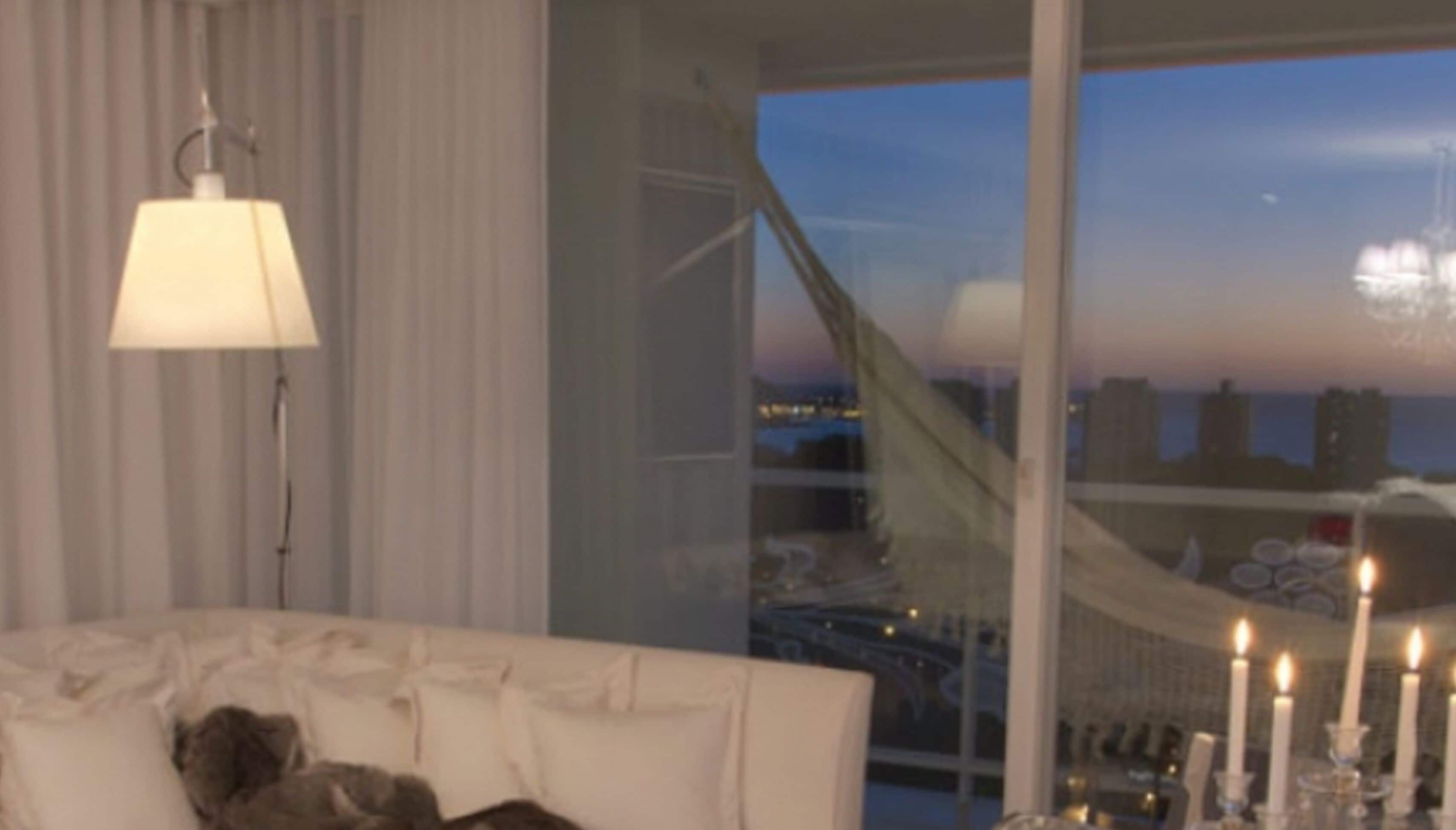 Een moderne hotelkamer met een groot raam met uitzicht op de stad, een bank en een lamp.