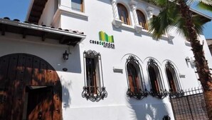 Un edificio con fachada blanca, una puerta de madera grande y tres ventanas de arco con rejas de metal.