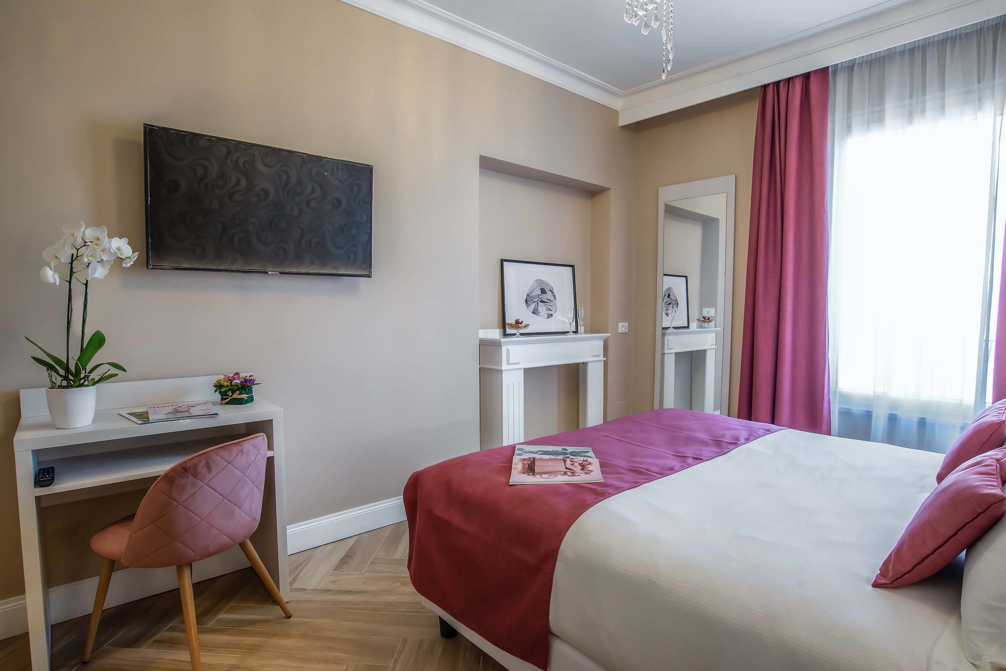 A hotel room with a bed, a desk, a chair, a TV, and a window with curtains.