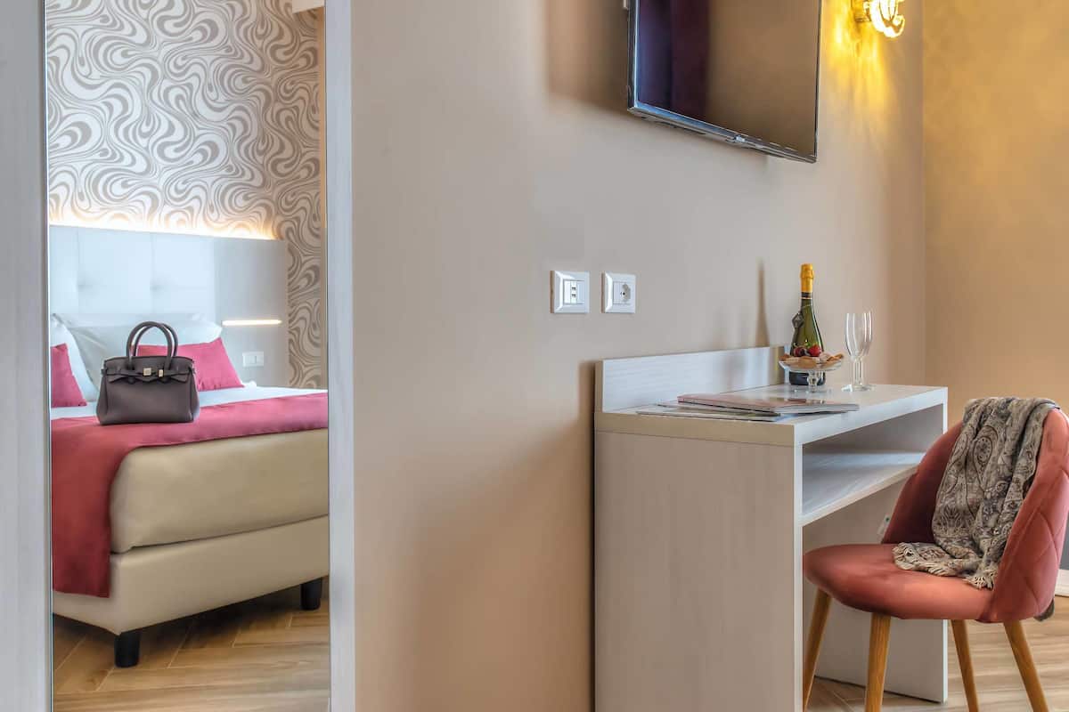 Et moderne hotelværelse med seng, skrivebord, stol og et fjernsyn hængt på væggen.