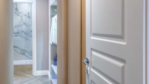 Un pasillo con pared de mármol, suelo de madera y una puerta blanca con picaporte plateado.
