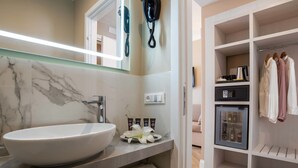 Un baño con lavamanos de mármol, un espejo, un teléfono y un mini refrigerador con botellas.