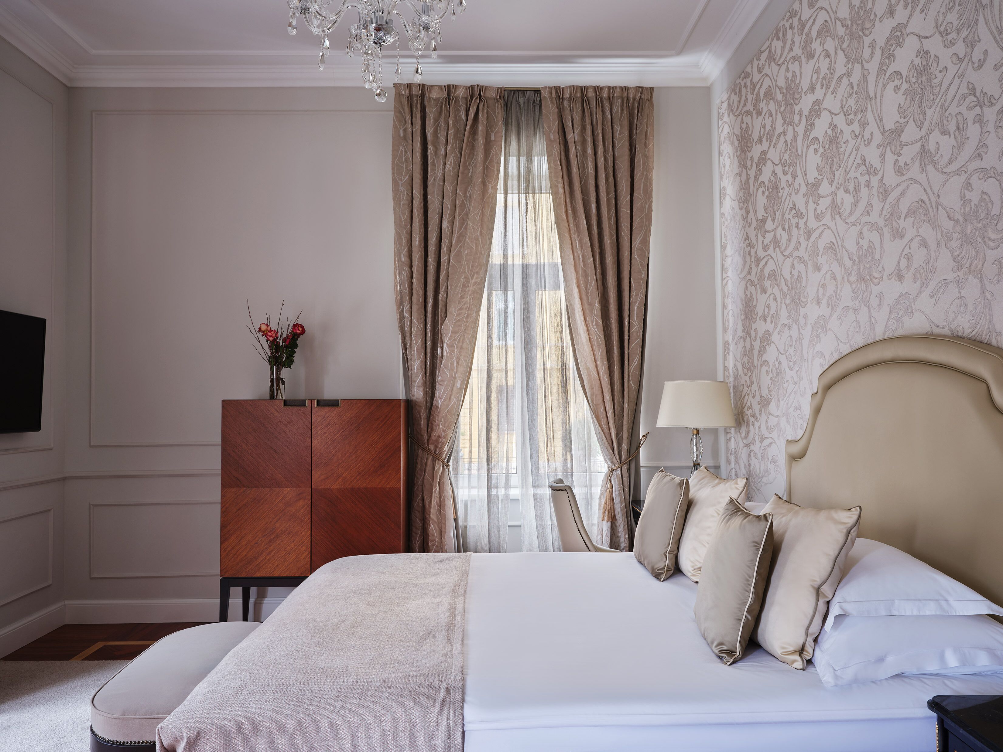 A hotel room with a bed, a desk, a lamp, and a chandelier.