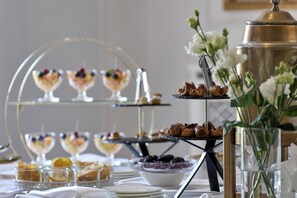 Een buffet met diverse desserts en gebak, waaronder een etagère met taarten en een schaal fruit.