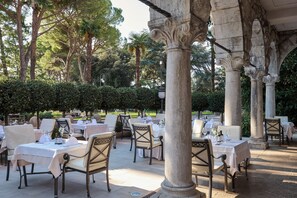 An outdoor dining area with tables and chairs, surrounded by stone columns and greenery. - Amadria Park Hotel Sveti Jakov (Opatija)