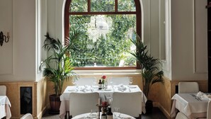 Ein Essbereich mit einem großen Bogenfenster, weiß gedeckten Tischen und einem Deckenfresko.