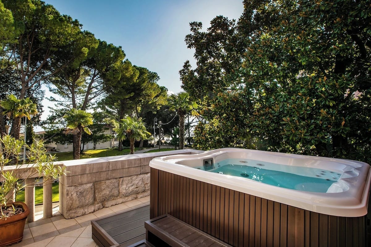 Un jacuzzi en un patio con barandas de piedra, rodeado de exuberante vegetación y árboles.