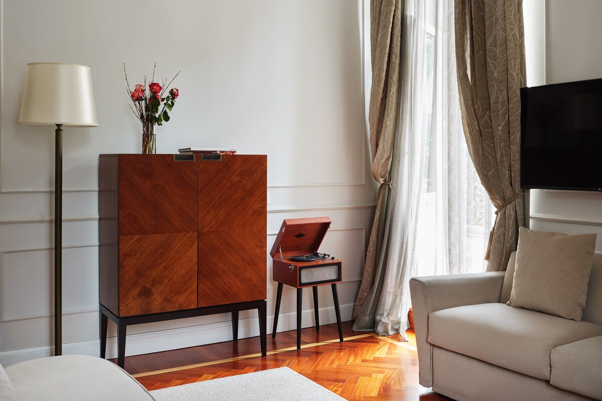 Una sala de estar moderna con un sofá, un aparador de madera, una lámpara de pie, una mesita con una radio y un televisor instalado en la pared.