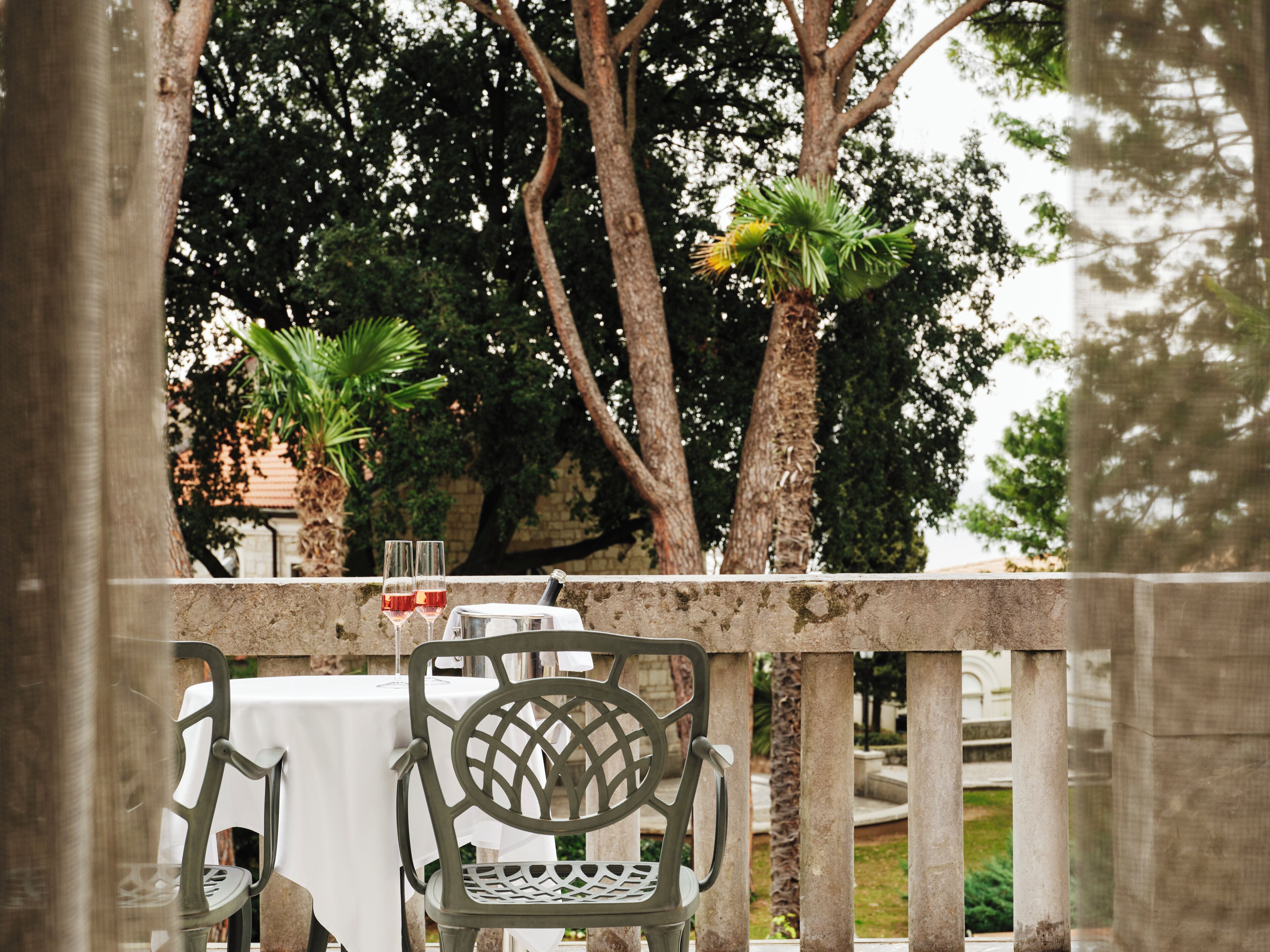 An outdoor dining area with a table and chairs, surrounded by trees and a stone wall.