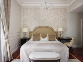 A bedroom with a large bed, two bedside tables with lamps, a chandelier, and a chair.