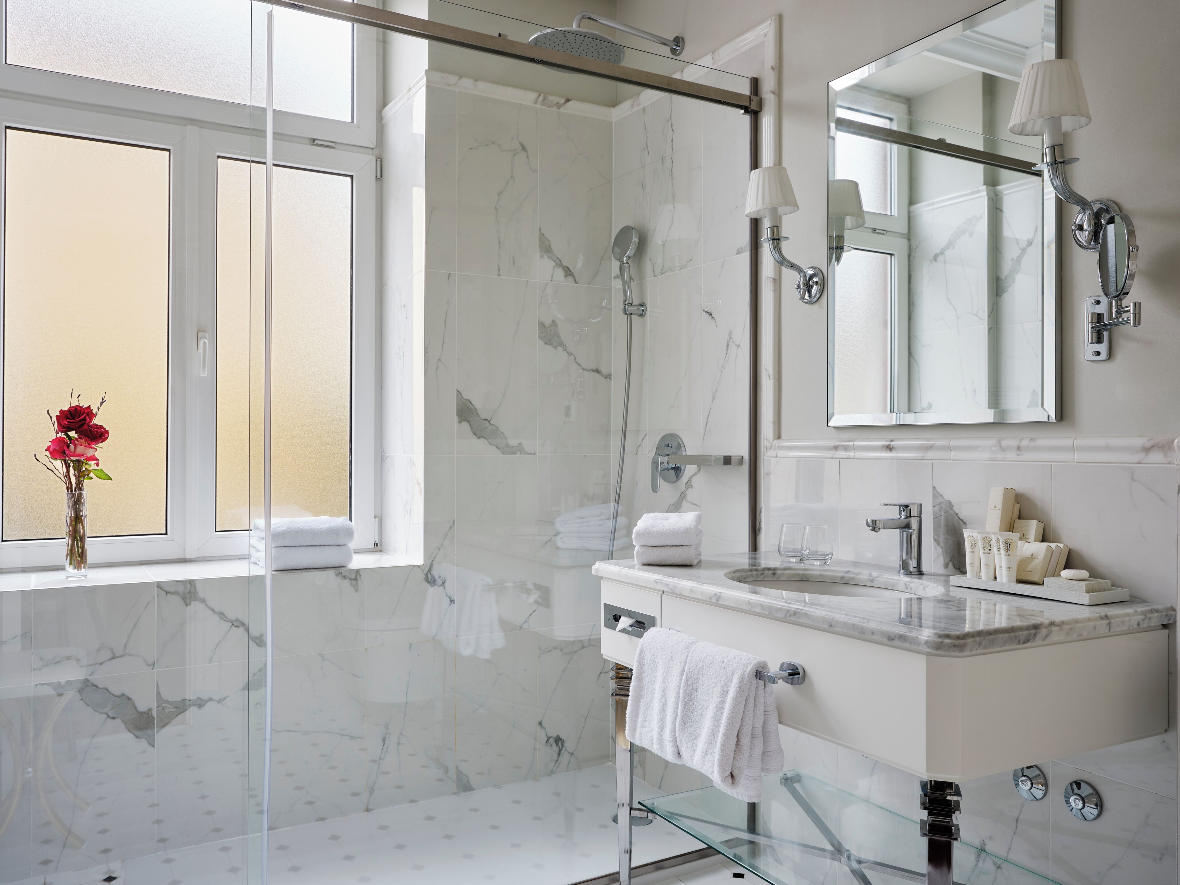 A modern bathroom with a glass shower enclosure, a large mirror, and a marble-tiled wall.