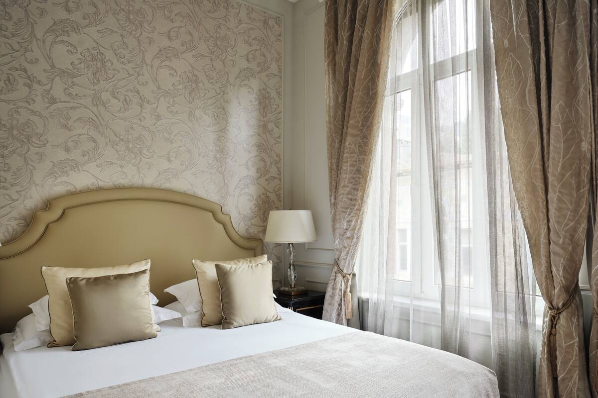 Una habitación de hotel con una cama grande, un papel tapiz decorado y cortinas translúcidas.