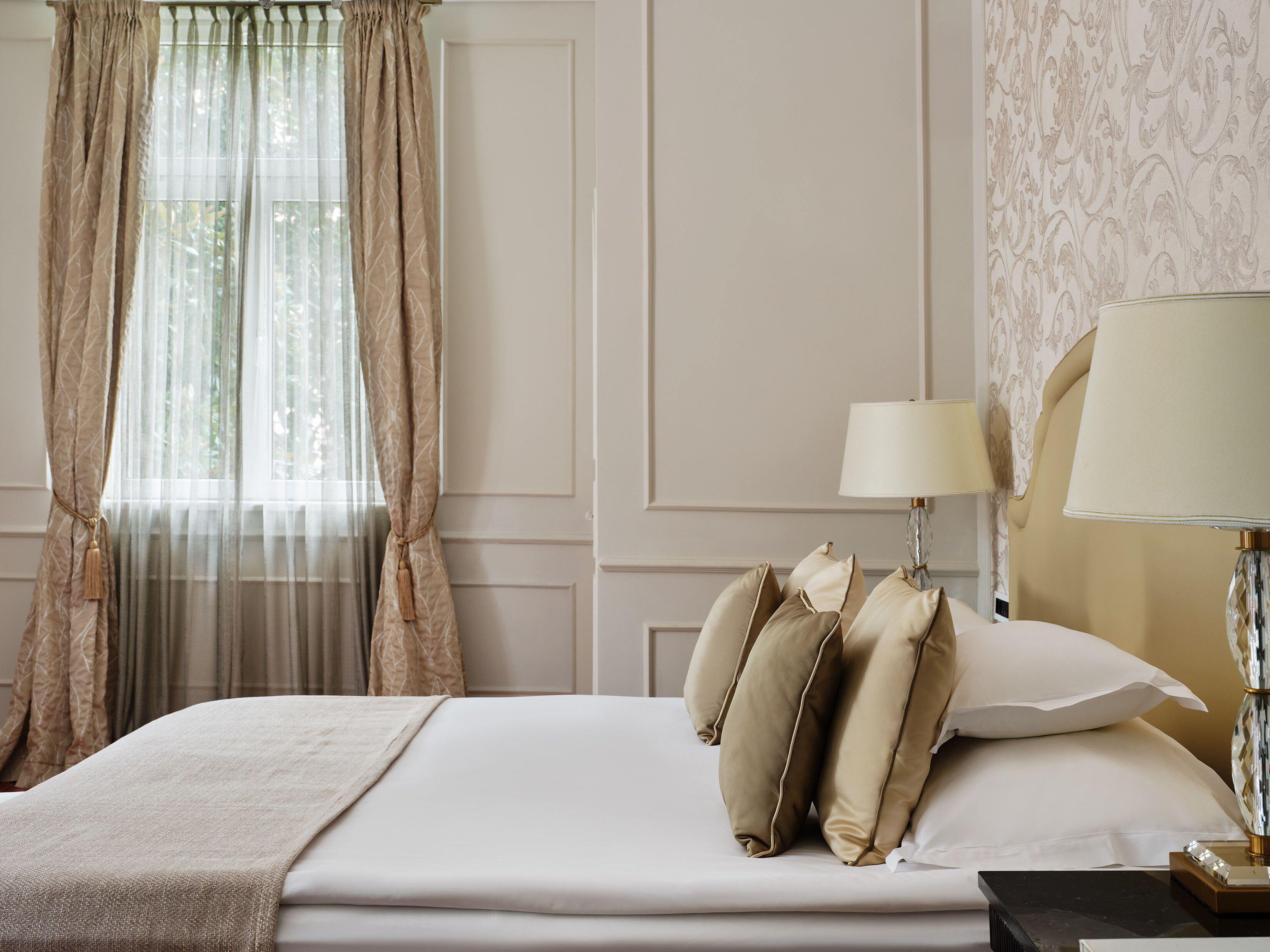 A neatly made bed with pillows, a lamp, and a window with curtains.