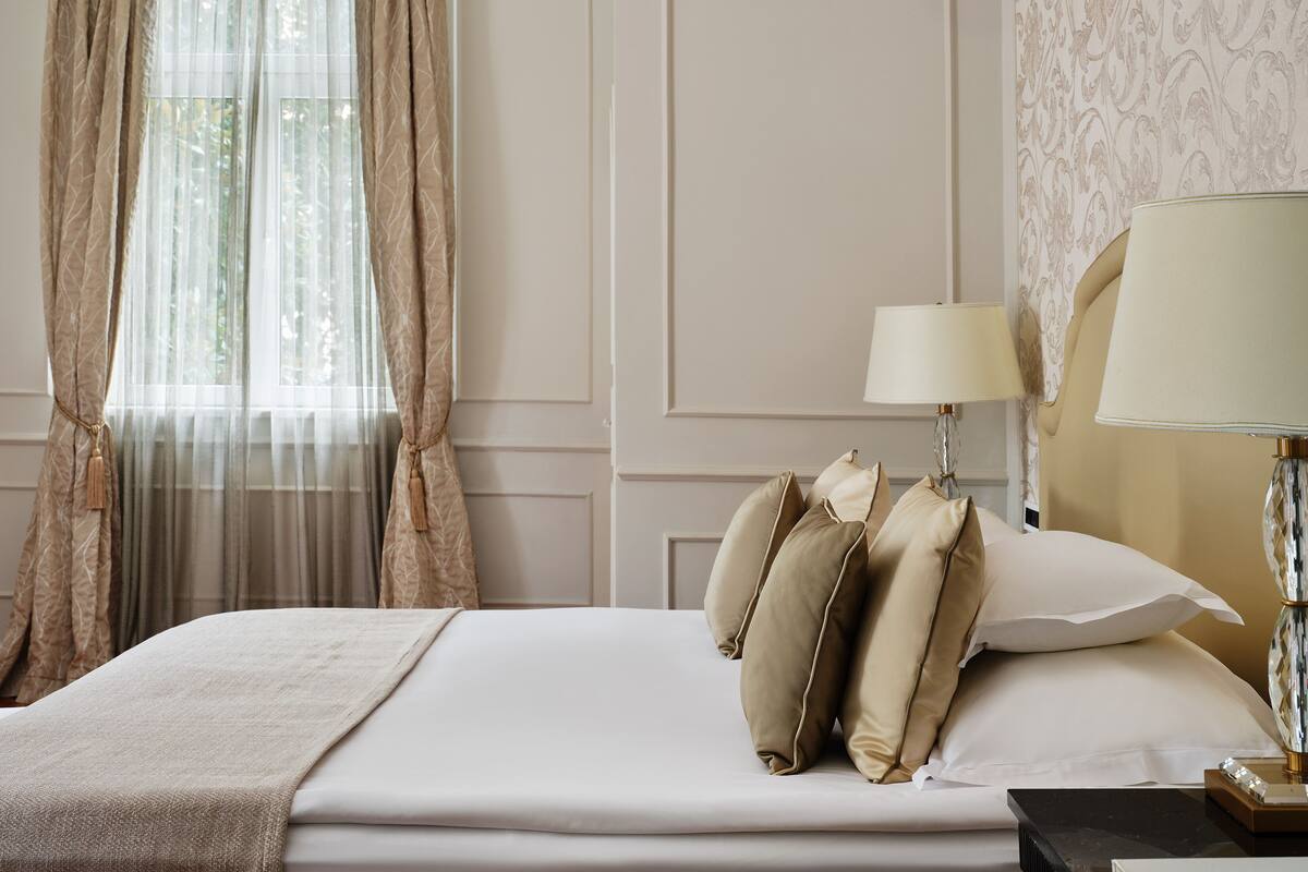 Una cama bien hecha con almohadas, una lámpara y una ventana con cortinas.