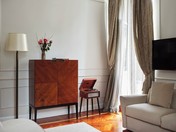 Una sala de estar moderna con un mueble de madera, una lámpara de pie, una mesita con una radio, un sofá y un televisor montado en la pared.