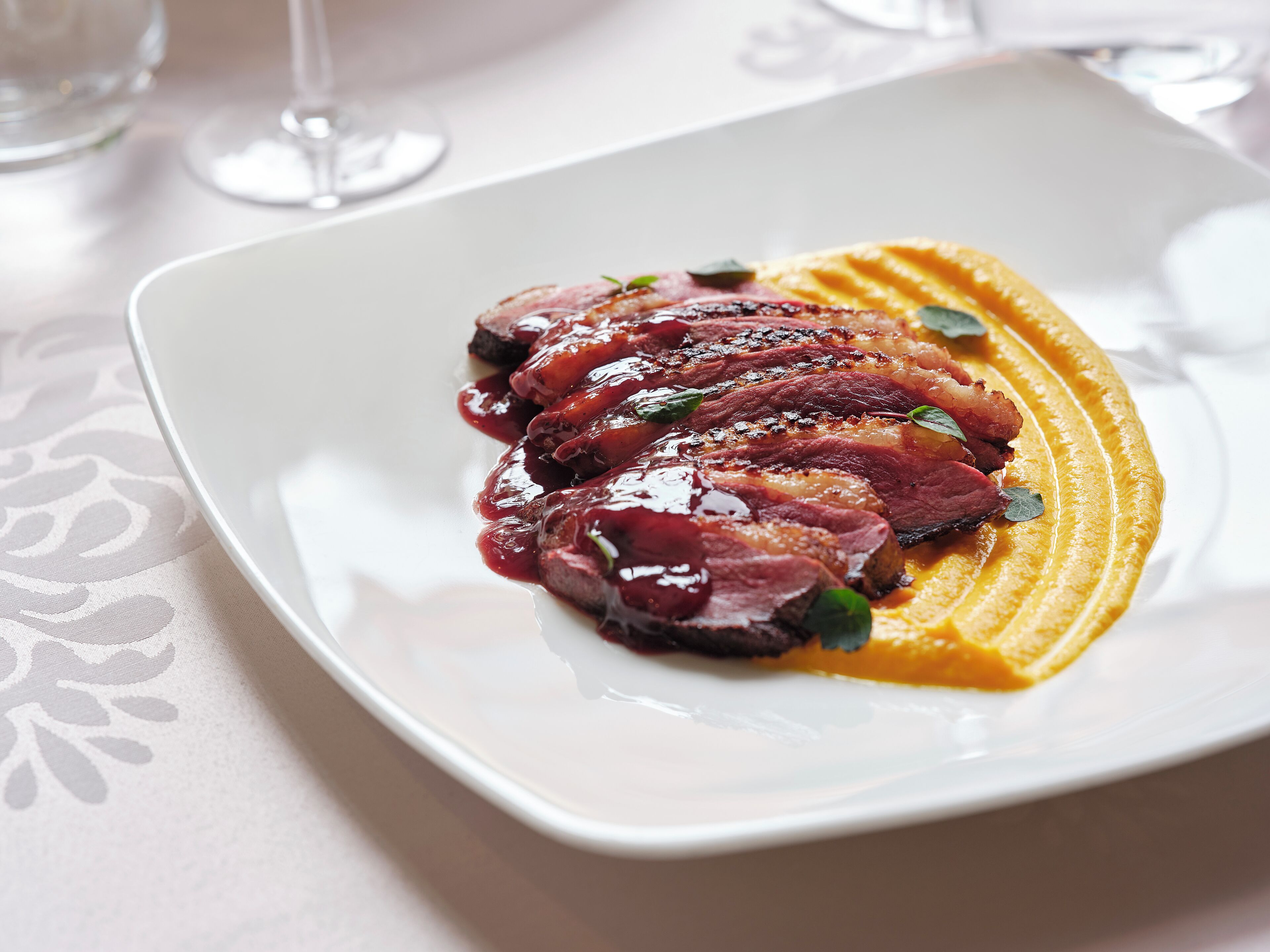 Un plato blanco con carne en rodajas y un puré amarillo como adorno.