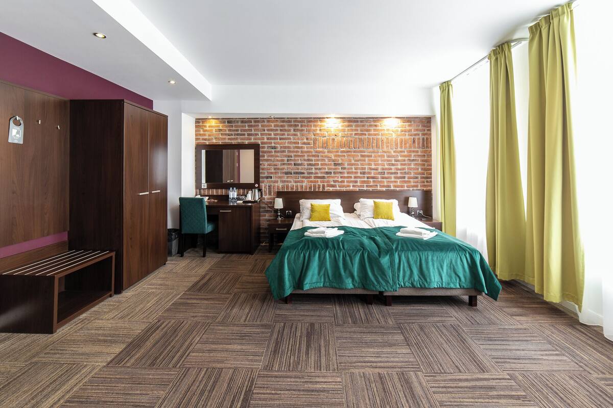 Hotellihuone, jossa on sänky, työpöytä, vaatekaappi ja tiiliseinä.