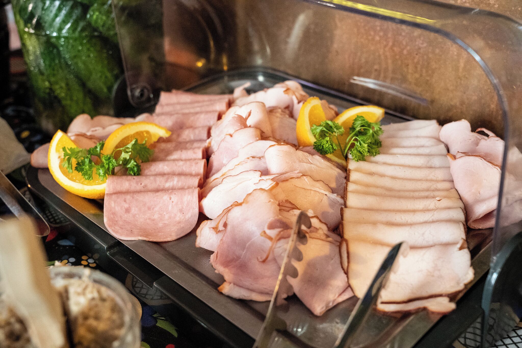 A glass display case with neatly arranged sliced meats, garnished with orange slices and parsley.