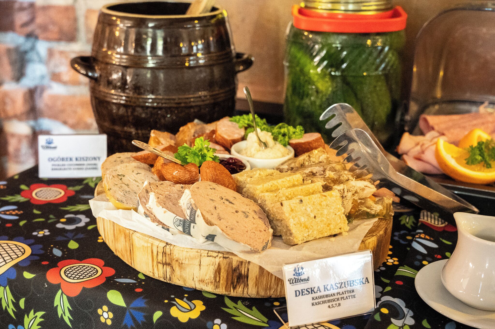 A wooden board with various food items, including sliced meats and cheeses, on a table with a floral tablecloth.