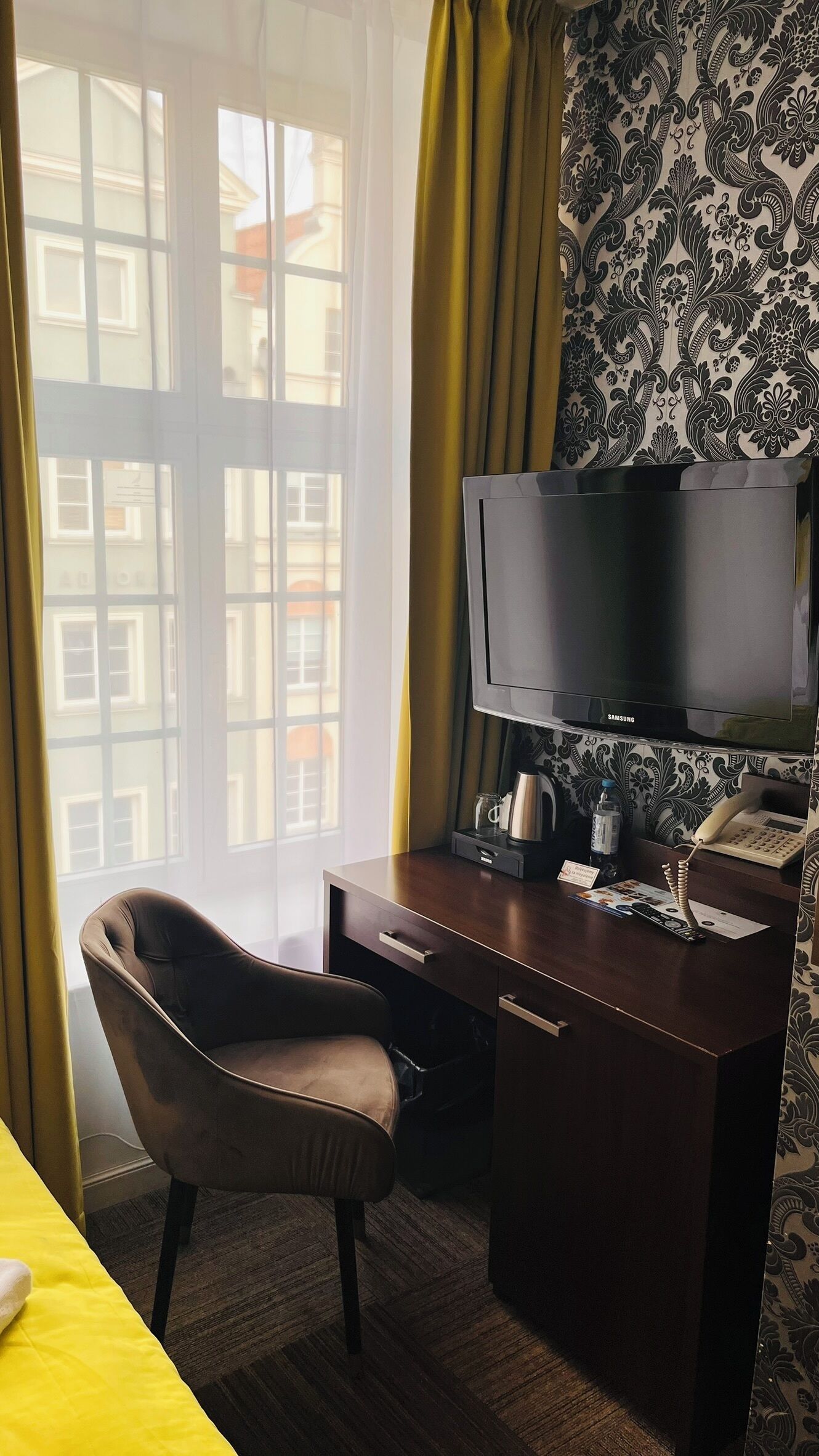 Ett hotellrum med en säng, ett skrivbord med en tv, en stol, en kaffebryggare och en telefon.